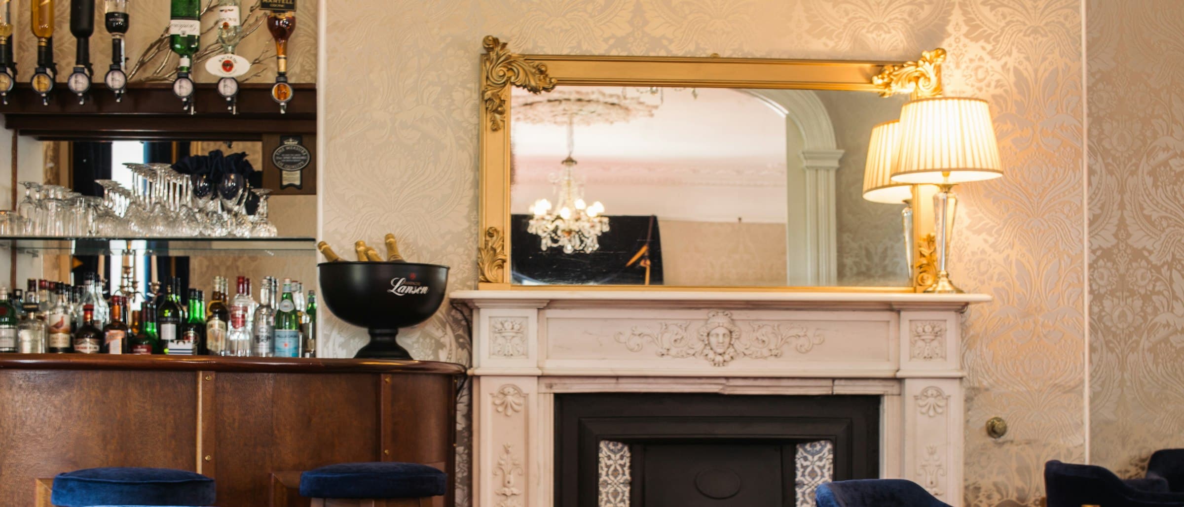 A hotel lounge with a marble fireplace, chandelier and bar.
