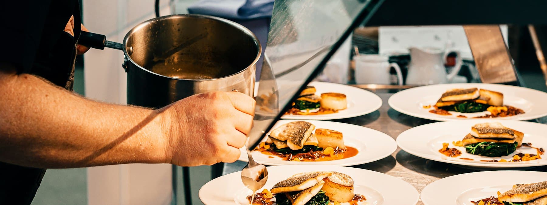 A chef finishing a row of plated dishes at the pass during service.